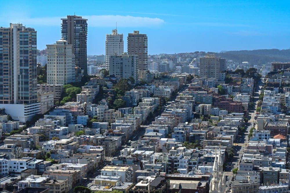 Panoramic view of San Francisco's hilly streets lined with residential buildings and skyscrapers under a clear blue sky.