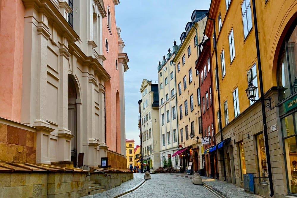 A view down a cobblestone street in Stockholm, Sweden, with a pink church on the left and colorful historic buildings on the right.