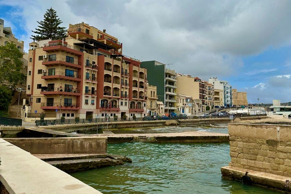 A tranquil canal scene in Gharsi, Malta, with apartment buildings and a small boat.