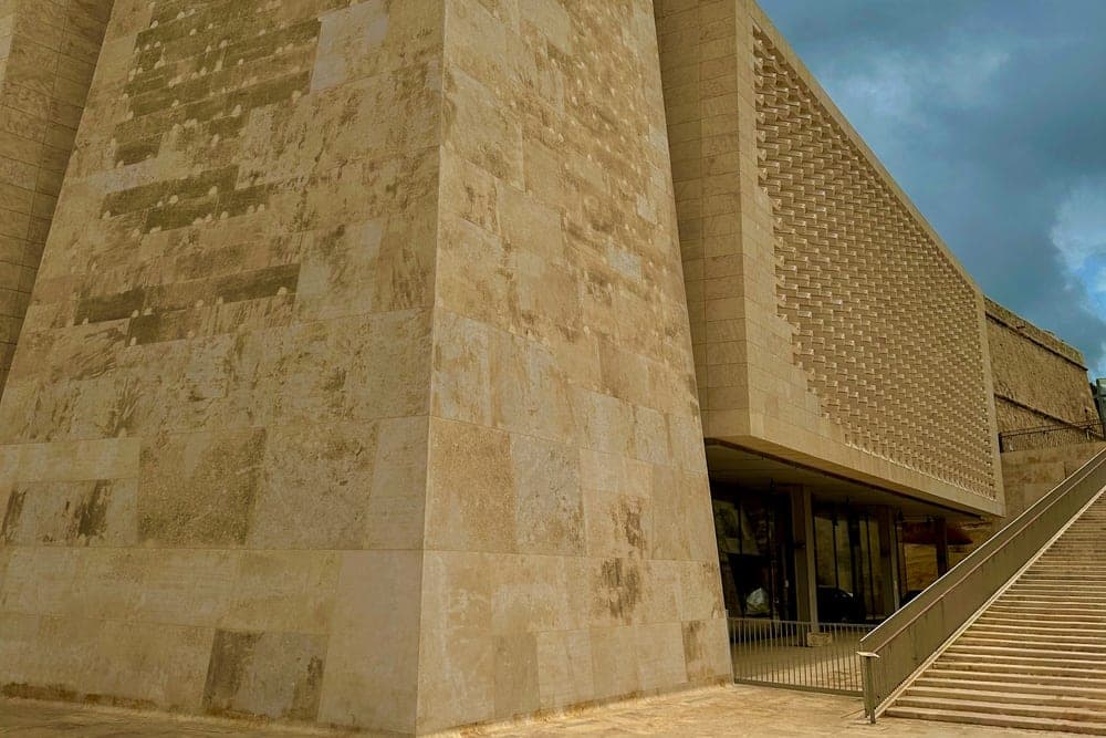 The modern Parliament building in Valletta, Malta, with its textured stone facade and distinctive geometric screen, under a cloudy sky.