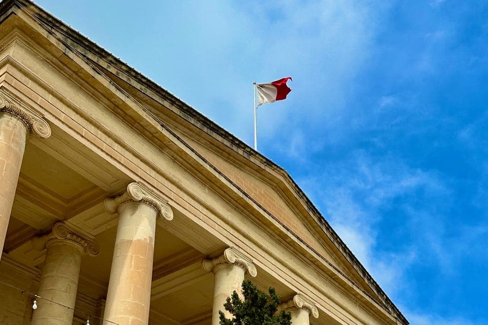 A grand neoclassical building with large columns and the Maltese flag flying high, in Valletta, Malta.