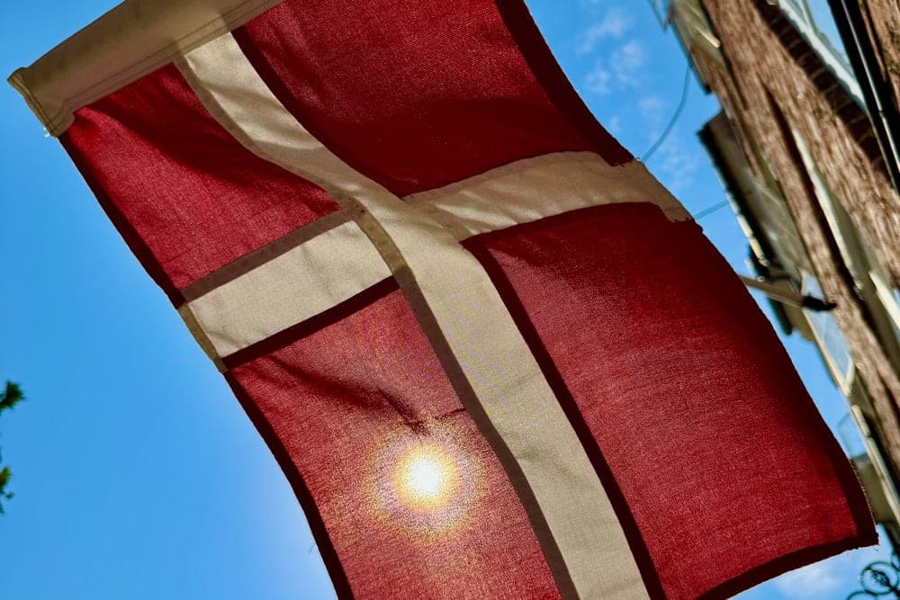 The Danish flag, Dannebrog, waving in the sun against a blue sky in Denmark.