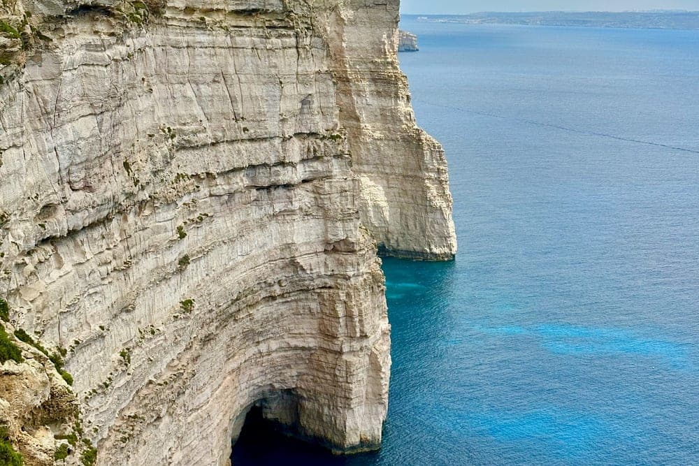 Towering white limestone cliffs at Gharsi, Malta, overlooking the deep blue Mediterranean Sea with a sea cave at its base.