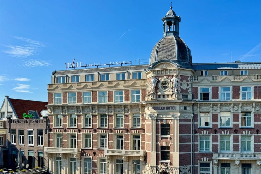 The ornate facade of the Tivoli Hotel on a canal in Amsterdam, Netherlands, under a clear blue sky.