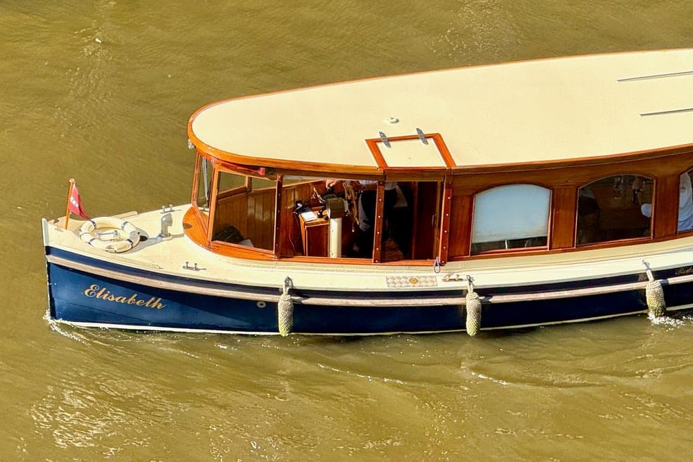 The classic canal boat 'Elisabeth' sails on a canal in Amsterdam, Netherlands, with its dark blue hull and wooden details visible.
