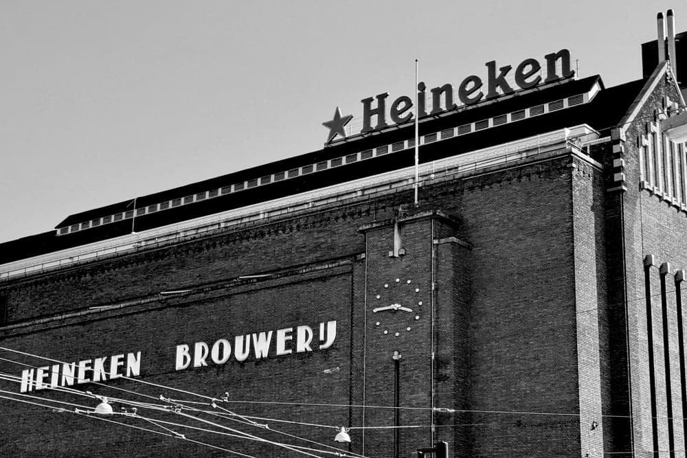 The historic Heineken Brewery building in Amsterdam, Netherlands, with its iconic signage and a large clock.