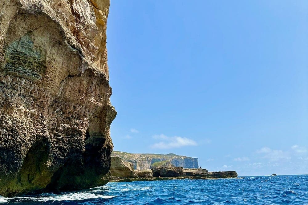 Rugged coastal cliffs of Malta rising from the deep blue Mediterranean Sea under a clear sky.