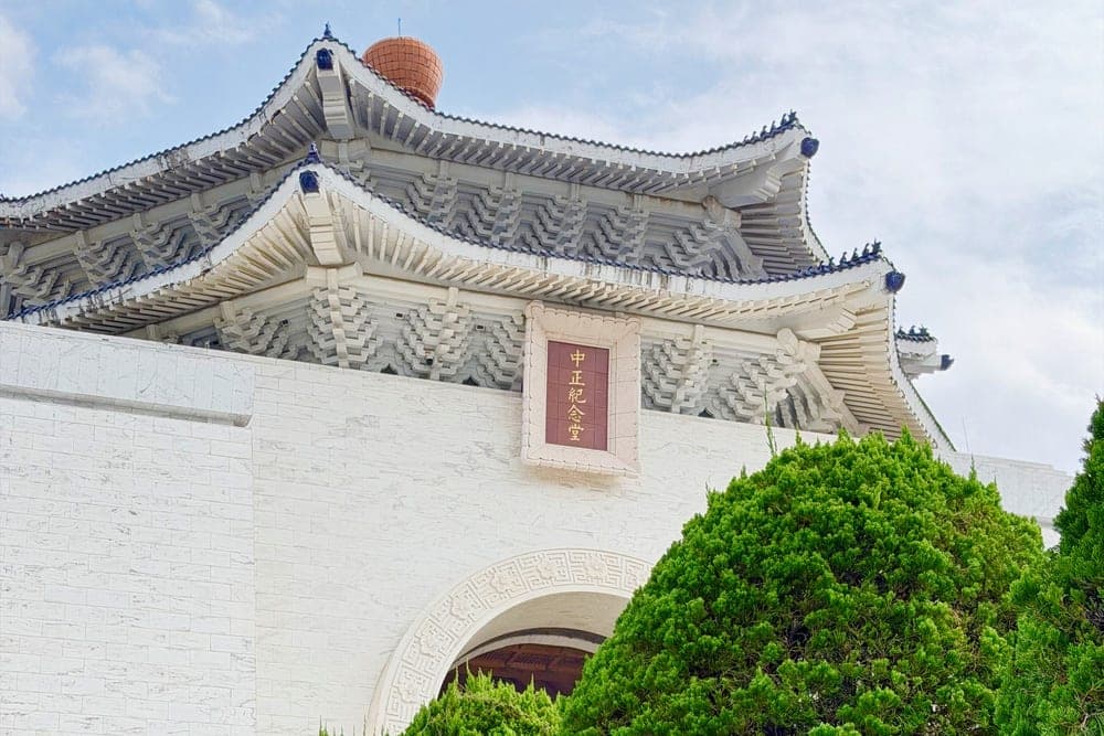 The Chiang Kai-shek Memorial Hall in Taipei, Taiwan, with its distinctive blue-tiled roof and white walls, framed by green bushes.