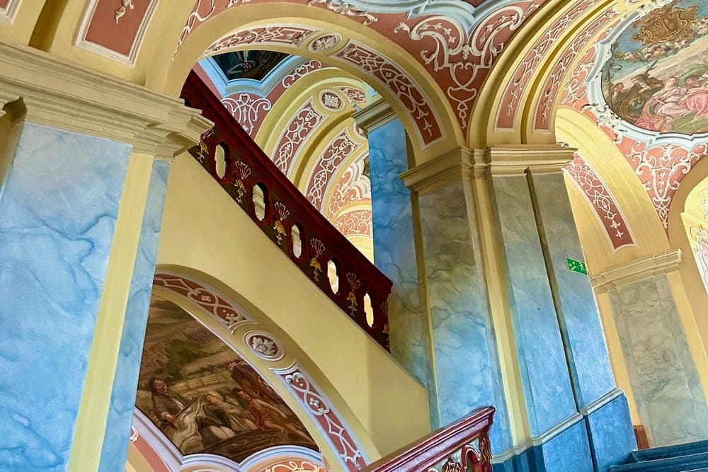 Ornate staircase with red banisters and painted ceilings in Wrocław, Poland.
