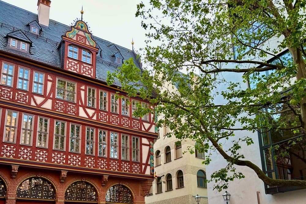 A charming square in Altstadt, Frankfurt, Germany, with a red and white timber-framed building, outdoor cafe seating, and people walking.