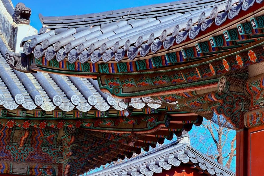Intricate details of traditional Korean architecture with colourful eaves and grey tiled roofs under a clear blue sky in Seoul, South Korea.