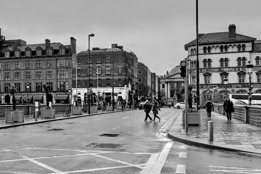 A street intersection in Dublin, Republic of Ireland, with pedestrians crossing and traditional buildings lining the road on an overcast day.