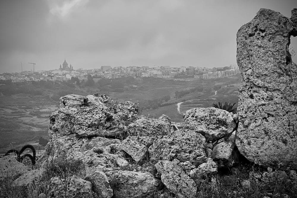 View of Xagħra, Malta, from ancient stone ruins under a cloudy sky.