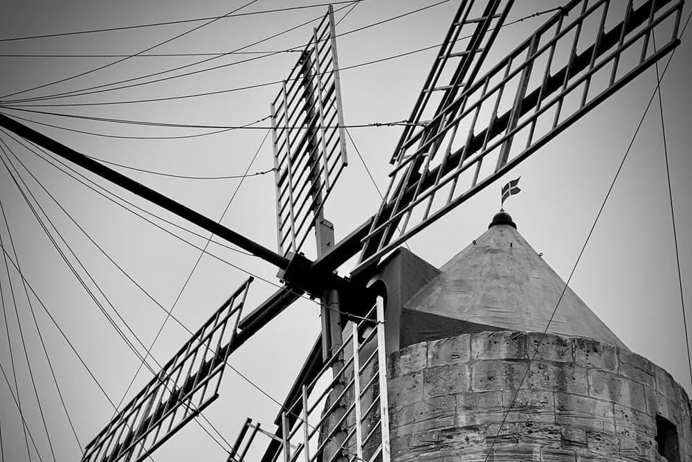 A black and white, low-angle view of a traditional windmill in Gharsi, Malta, focusing on its large sails and stone tower.
