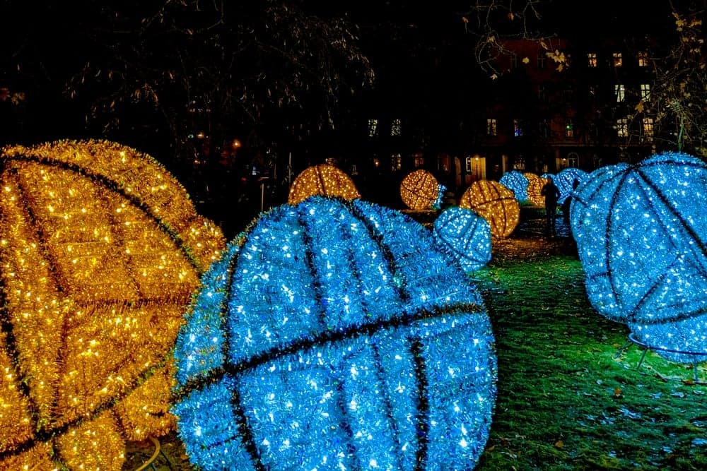Spherical light installations in gold and blue illuminate a park at night in Wrocław, Poland.