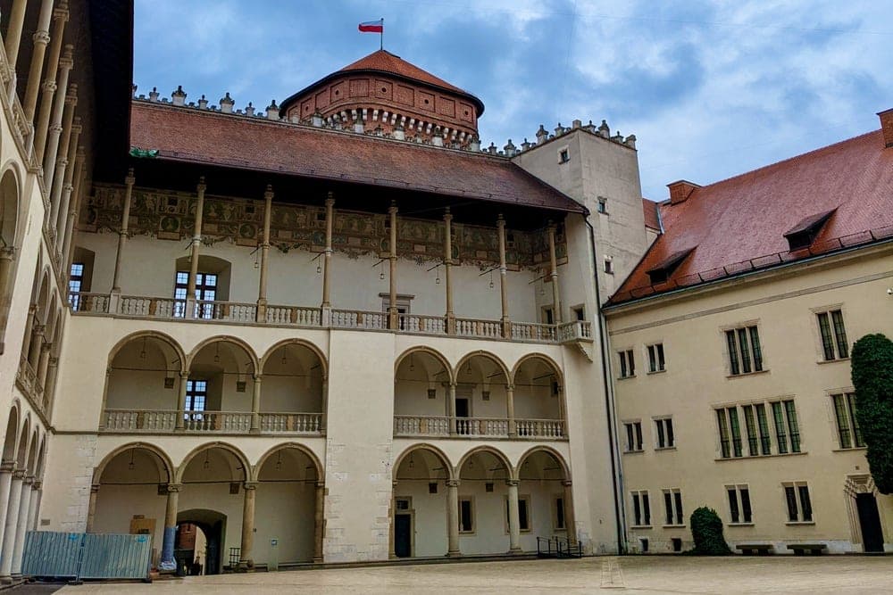 Courtyard of Wawel Castle in Krakow, Poland, with arcaded walkways and a round tower under a cloudy sky.
