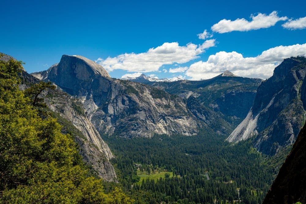 Panoramic view of Yosemite Valley, Yosemite National Park, California, United States, featuring Half Dome and dense pine forests under a blue sky with clouds.