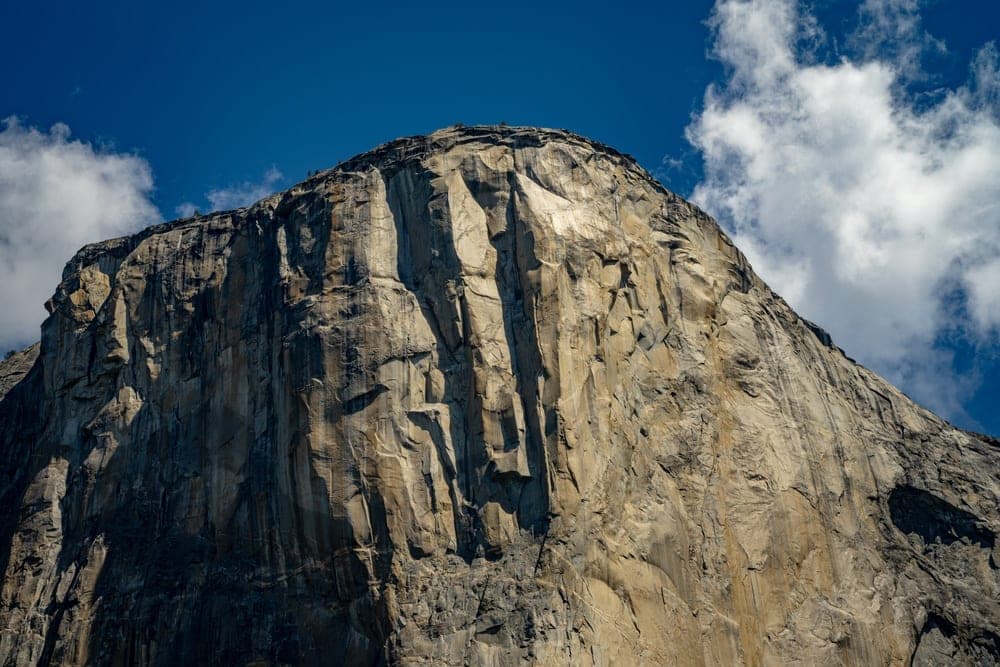 The monumental granite face of El Capitan in Yosemite National Park, California, United States, under a bright blue sky with scattered clouds.