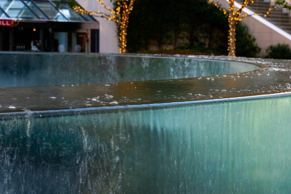 A curved water feature with cascading water in San Francisco, United States, with illuminated trees in the background.