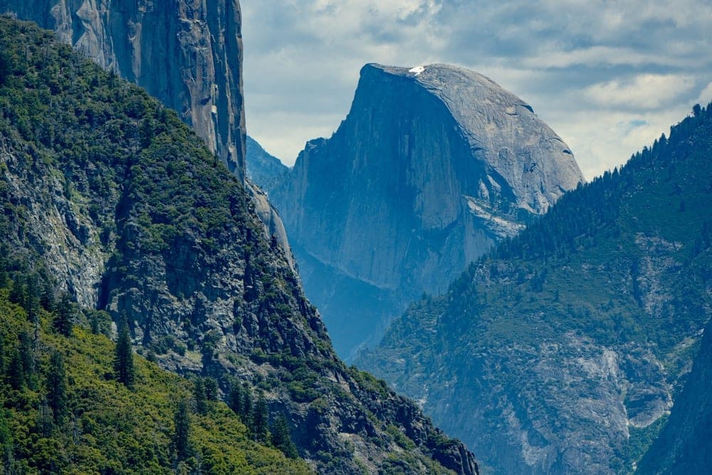 A view of El Capitan and Half Dome in Yosemite National Park, United States, under a partly cloudy blue sky.