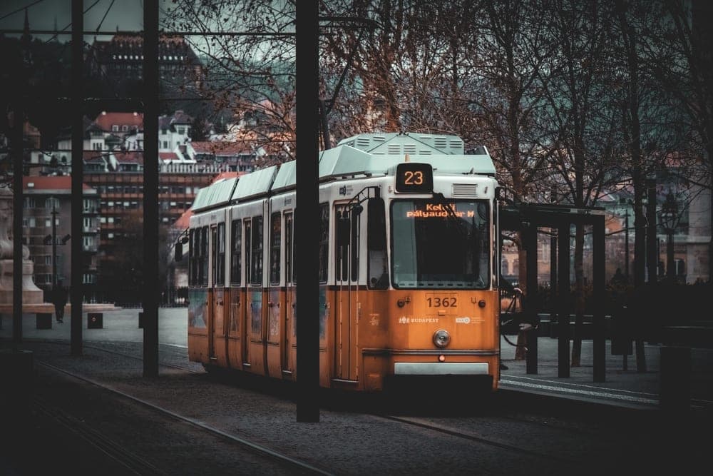 A yellow tram numbered 23 on a street in Budapest, Hungary, with buildings and bare trees in the background.
