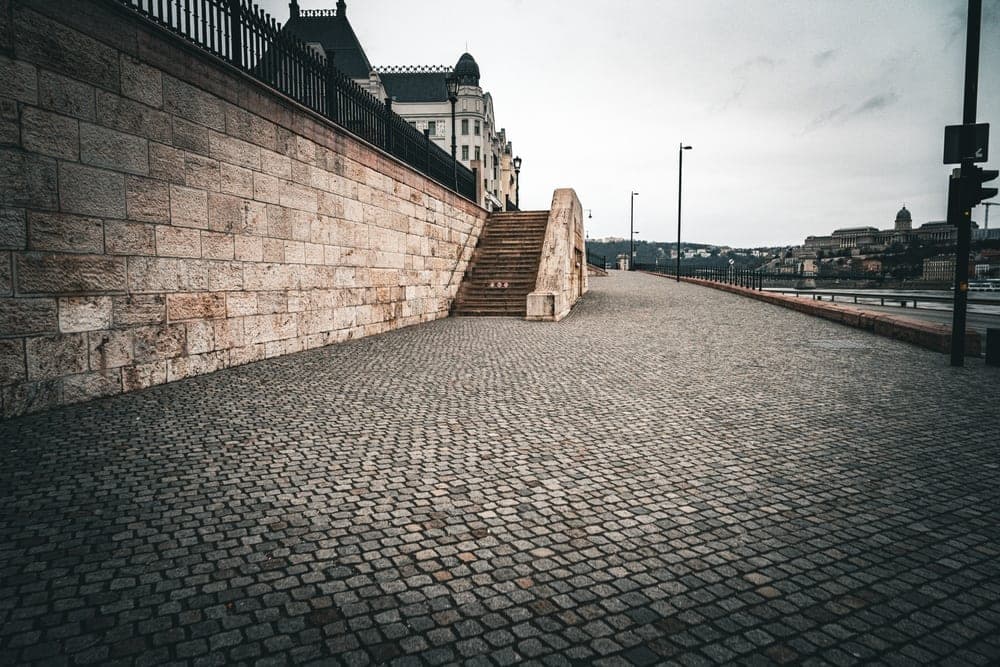 Cobblestone pathway and stone wall leading to stairs in Budapest, Hungary, with Buda Castle in the distance.