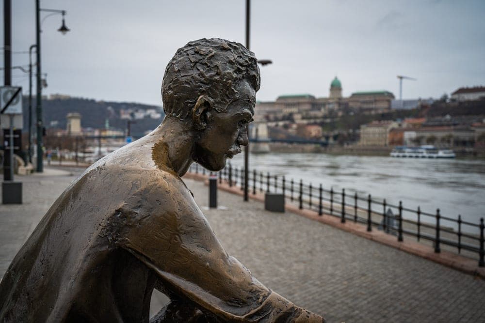 Bronze statue of a man looking out over the Danube River in Budapest, Hungary, with the Buda Castle complex in the background.