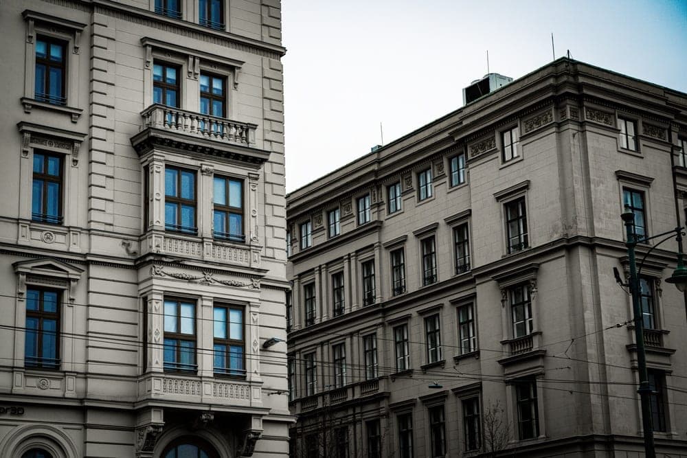 Two ornate, pale stone buildings with dark windows on Id. Antall József Rakpart in Budapest, Hungary, under an overcast sky.