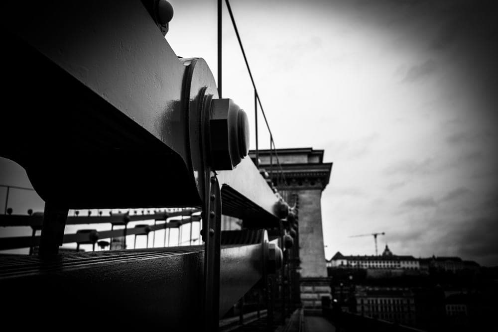 Close-up of the riveted iron structure of the Széchenyi Chain Bridge in Budapest, Hungary, with a bridge tower in the background.