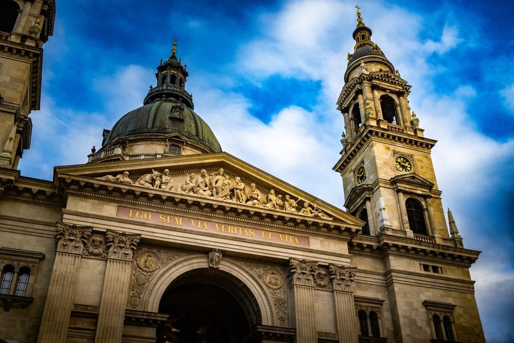 St. Stephen's Basilica in Budapest, Hungary, with its bell tower and dome against a dramatic blue sky with white clouds.