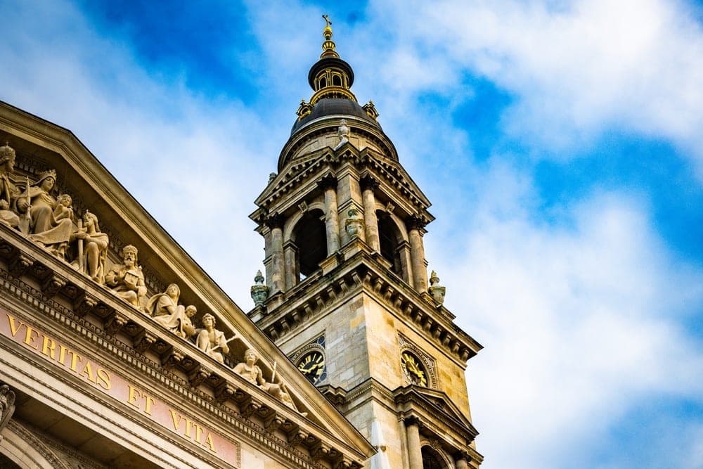 The St. Stephen's Basilica in Budapest, Hungary, viewed from a low angle against a bright blue sky.