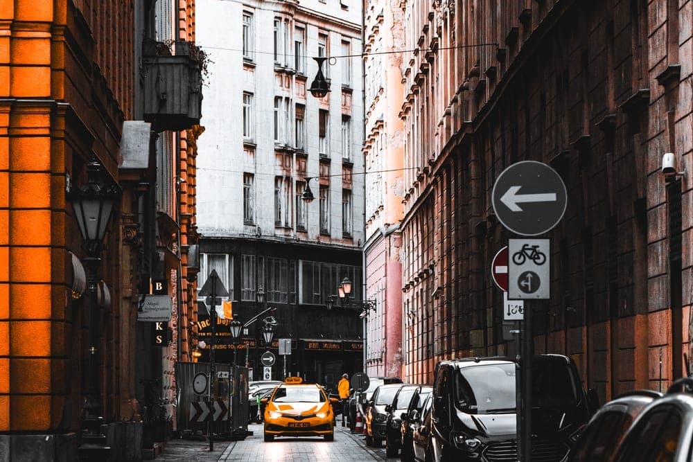 A yellow taxi drives down a narrow street in Budapest, Hungary, lined with historic buildings.