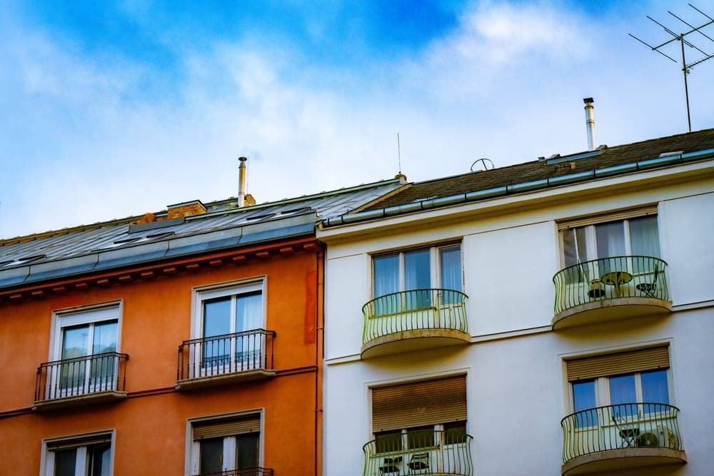Orange and white apartment buildings with wrought-iron balconies under a bright blue sky in Budapest, Hungary.