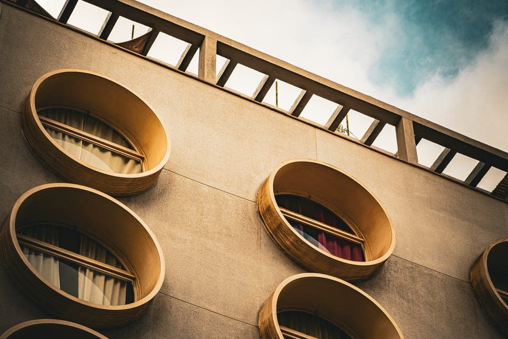 A modern building facade in Barcelona, Spain, with circular windows and a concrete lattice structure against a cloudy sky.