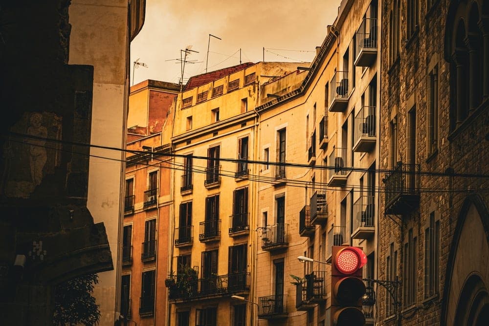 A street in El Barri Gòtic, Barcelona, Spain, with historic buildings, a red traffic light, and overhead wires.