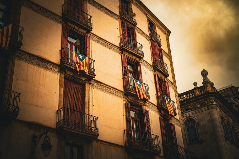 Catalan flags hang from balconies on a historic building in Barcelona, Spain, under a dramatic sky.