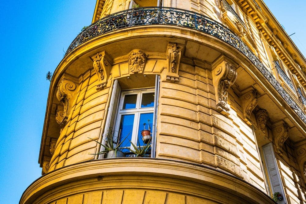 Ornate yellow building facade in Marseille, France, with a curved corner, balconies, and blue sky.