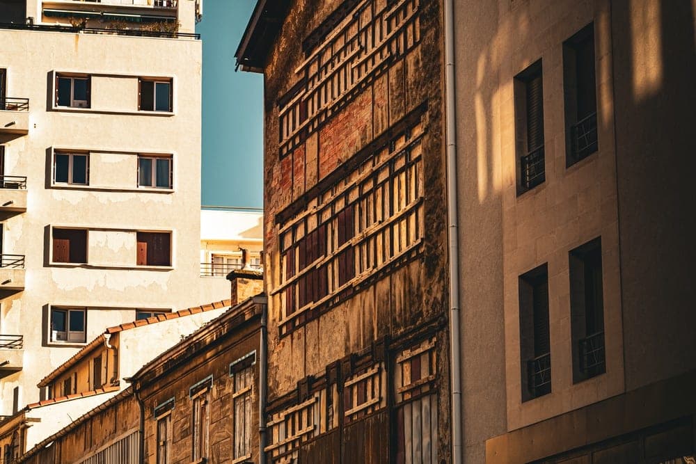 A street scene in Marseille, France, showing a contrast between old and new buildings with strong sunlight and shadows.