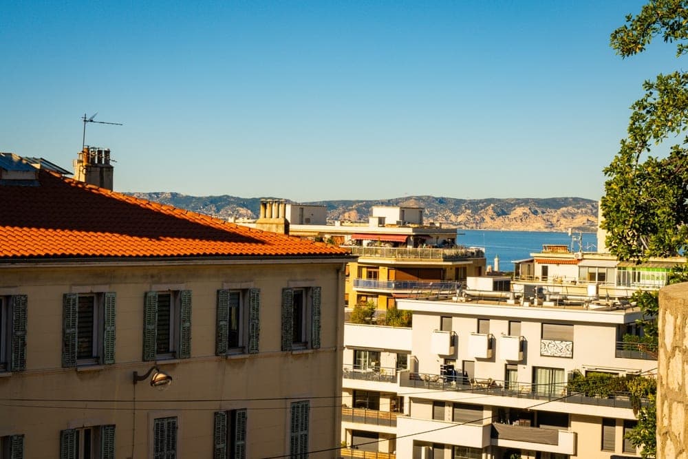 View of urban rooftops and the Mediterranean Sea in Marseille, France, under a clear blue sky.