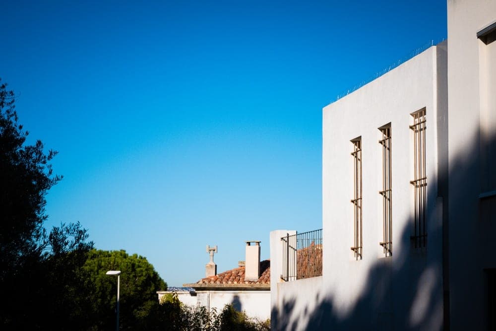 Modern white building facade with three barred windows against a clear blue sky, in Marseille, France.