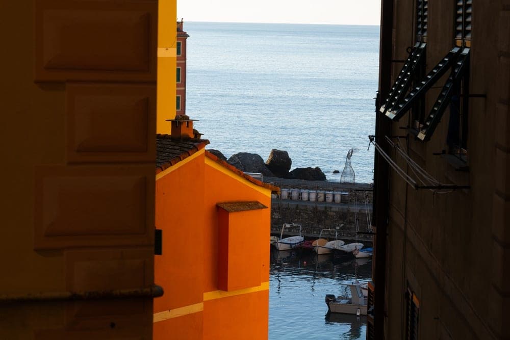 A narrow alleyway view of a small harbour in Camogli, Genoa, Italy, with colourful buildings and moored boats.