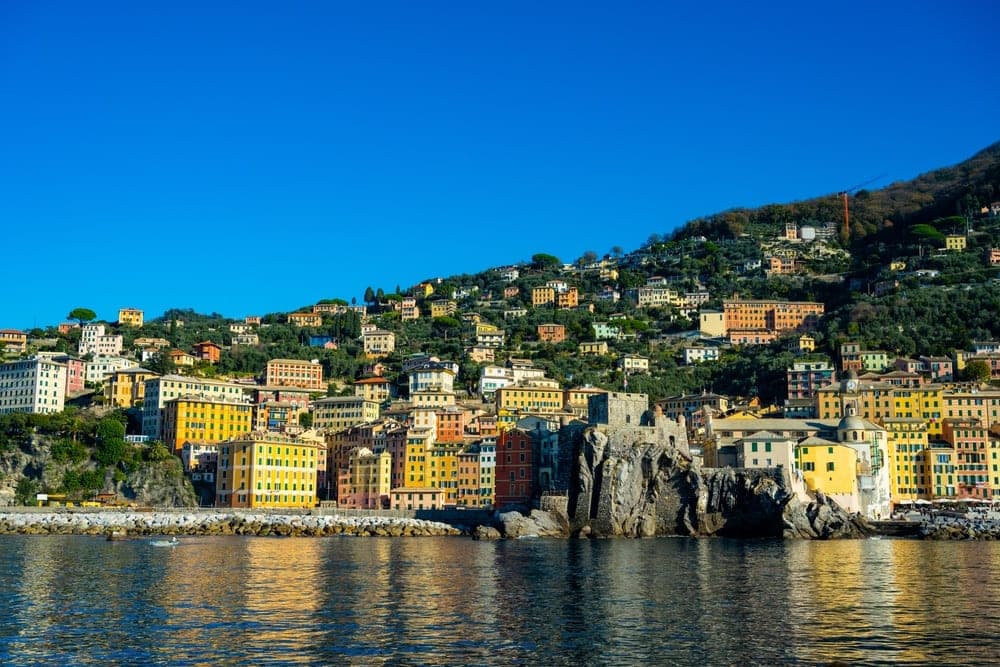 The vibrant, colourful buildings of Camogli, Italy, cascading down a steep green hillside towards the Ligurian Sea.