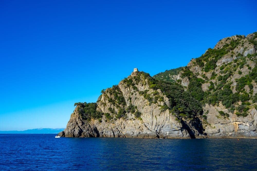 A stone tower stands atop a steep, green cliff overlooking the blue sea at Portofino, Italy.