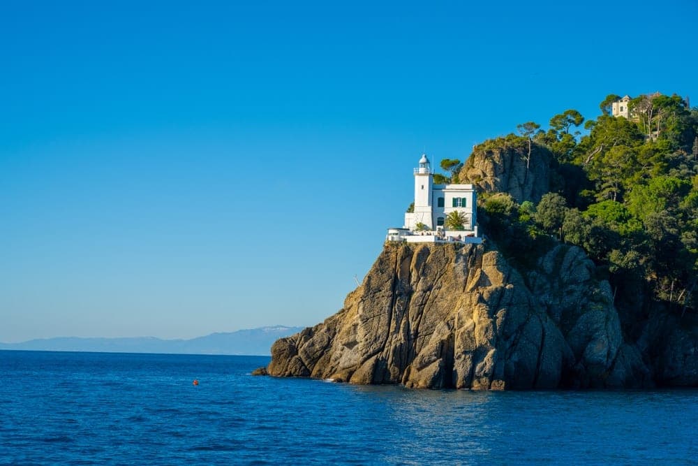 The white lighthouse of Portofino, Italy, perched on a rugged cliff overlooking the deep blue sea.