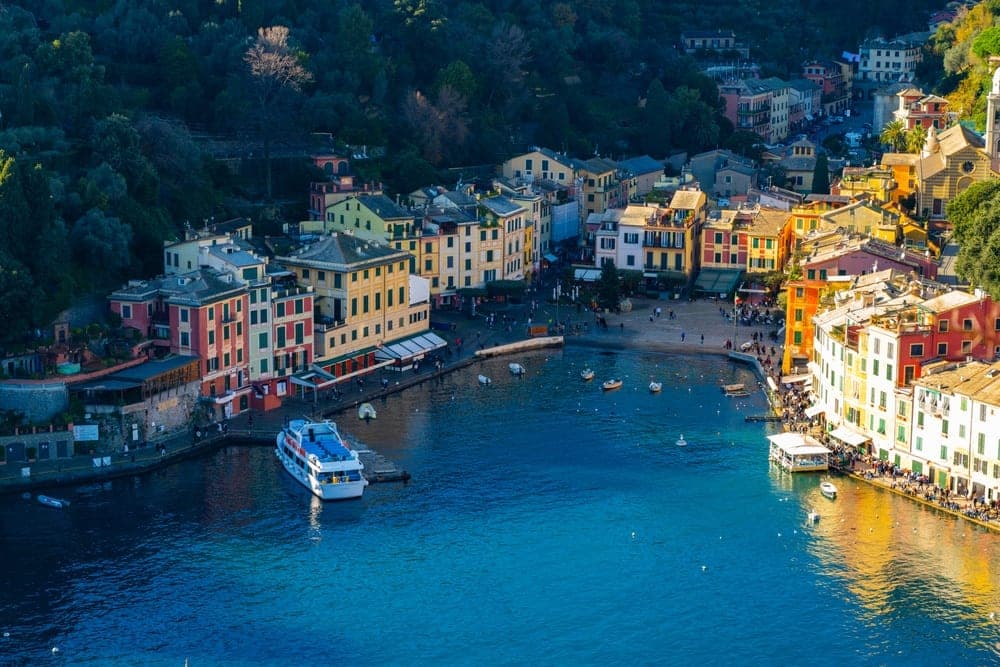 A vibrant aerial view of the harbor in Portofino, Italy, with colorful buildings lining the water and boats docked.