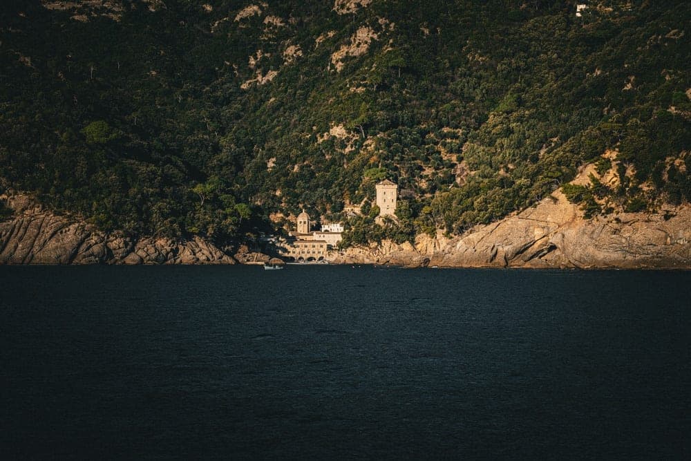 A historic complex of buildings and a watchtower on a forested mountainside above the sea in Portofino, Italy.