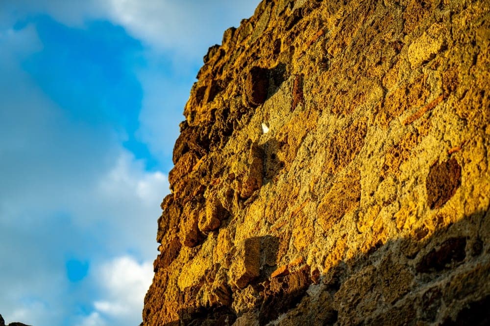 A sunlit ancient stone wall in Pompeii, Italy, against a bright blue sky.