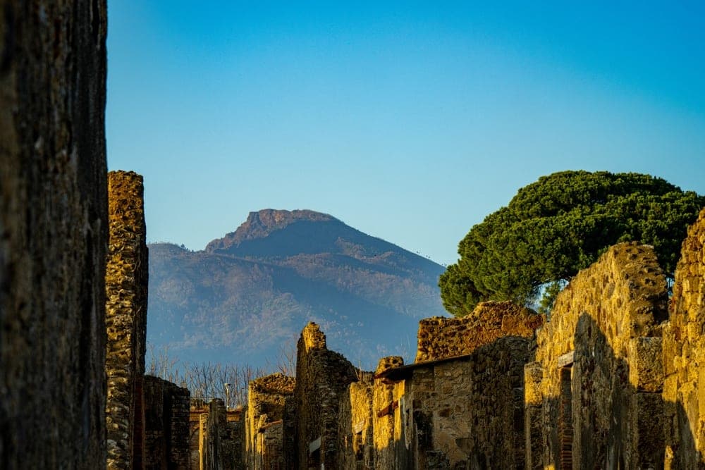 Ancient Roman ruins in Pompeii, Italy, with Mount Vesuvius in the background under a clear blue sky.
