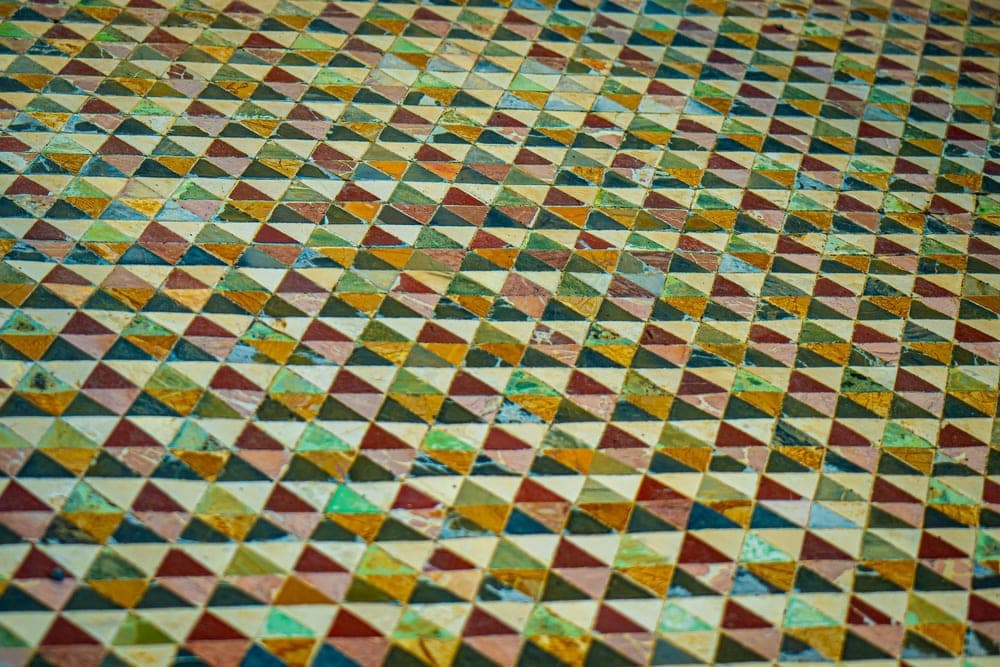Intricate geometric mosaic floor in Pompeii, Italy, with triangular tesserae in earthy colors.