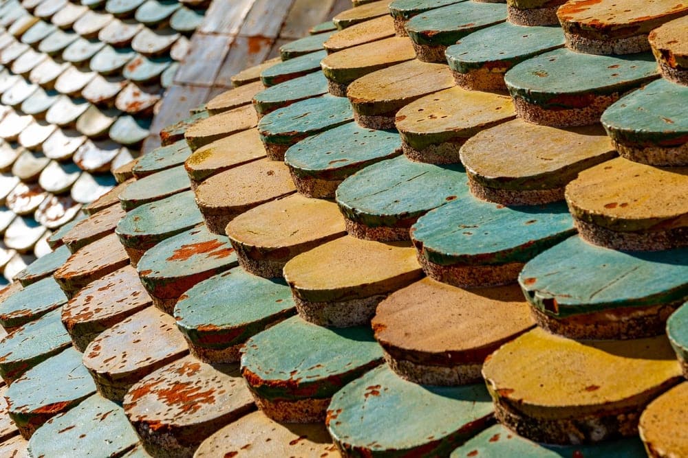 Close-up of weathered, scale-like terracotta, yellow, and green tiles on a historic roof in Palermo, Italy.